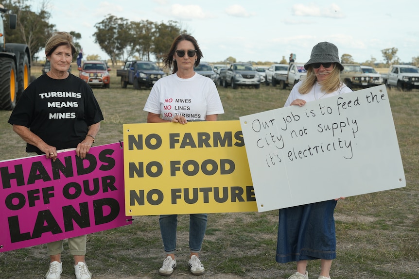 Three women holding signs on farm reading: "hands off our land", "no farms no food no future" and "our job is to feed the.."