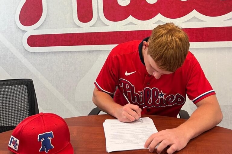 A young man in a phillies shirt signing a paper