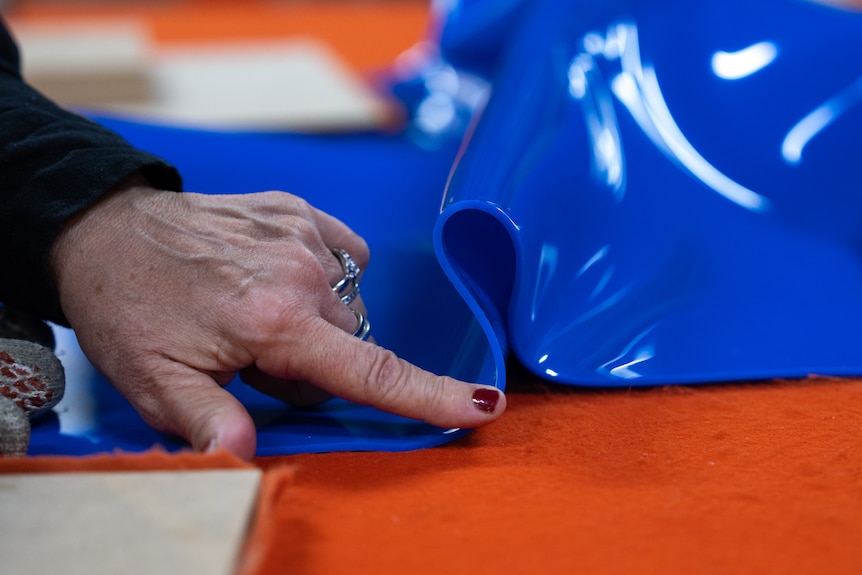 A woman's hand rests on a crumbled sheet of blue plastic.