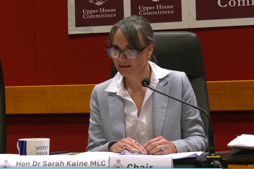 Woman in a grey suit wearing glasses.