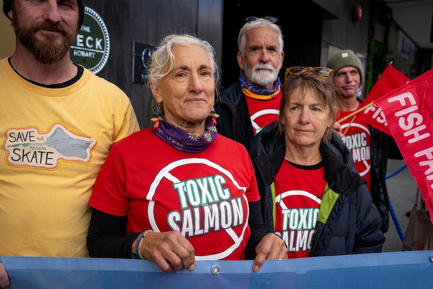 Two women and three men wearing t-shirts that red "toxic salmon" stand in a group