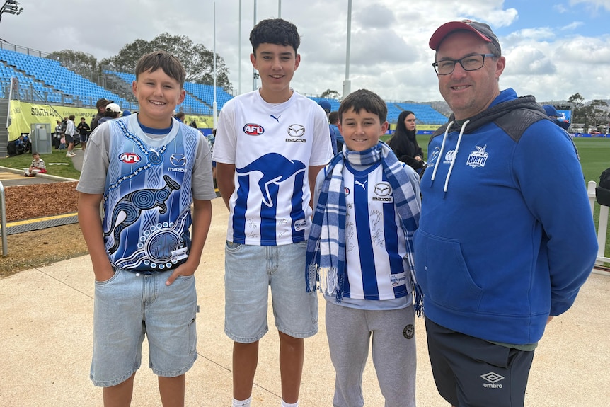 Three boys and a man wearing North Melbourne gear