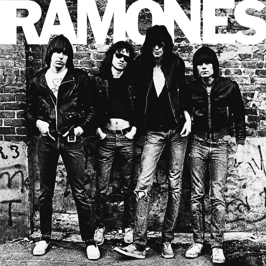 Black-and-white photo of four Ramones members in leather jackets against a graffiti brick wall, RAMONES text above