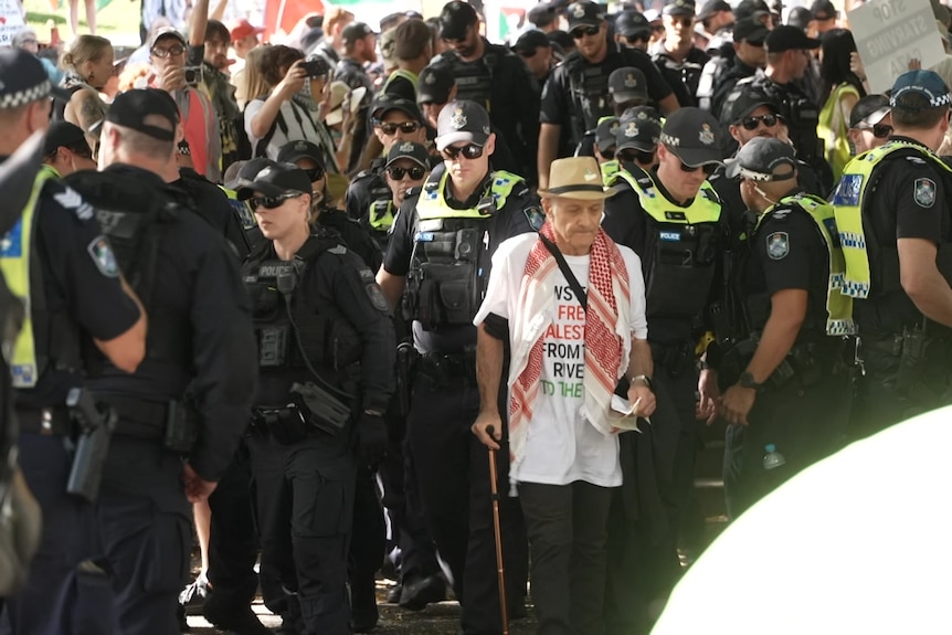 A man with a cane being led by police