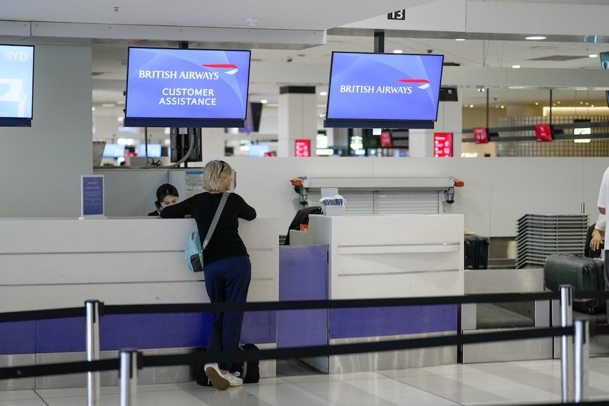 A woman stands at the British Airways check-in counter.