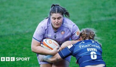 Maud Muir runs into a tackle while holding a rugby ball under her right arm to her body, as Delaney Burns (Bristol Bears) crouches and holds an arm around Muir's waist