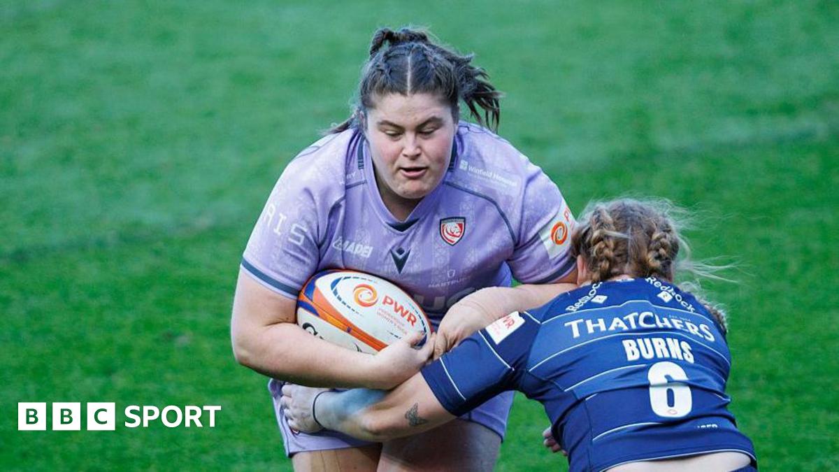 Maud Muir runs into a tackle while holding a rugby ball under her right arm to her body, as Delaney Burns (Bristol Bears) crouches and holds an arm around Muir's waist