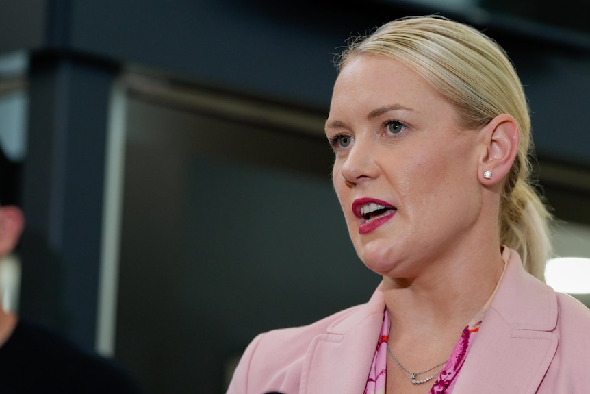 A close up shot of a blonde woman wearing a pink blazer while speaking