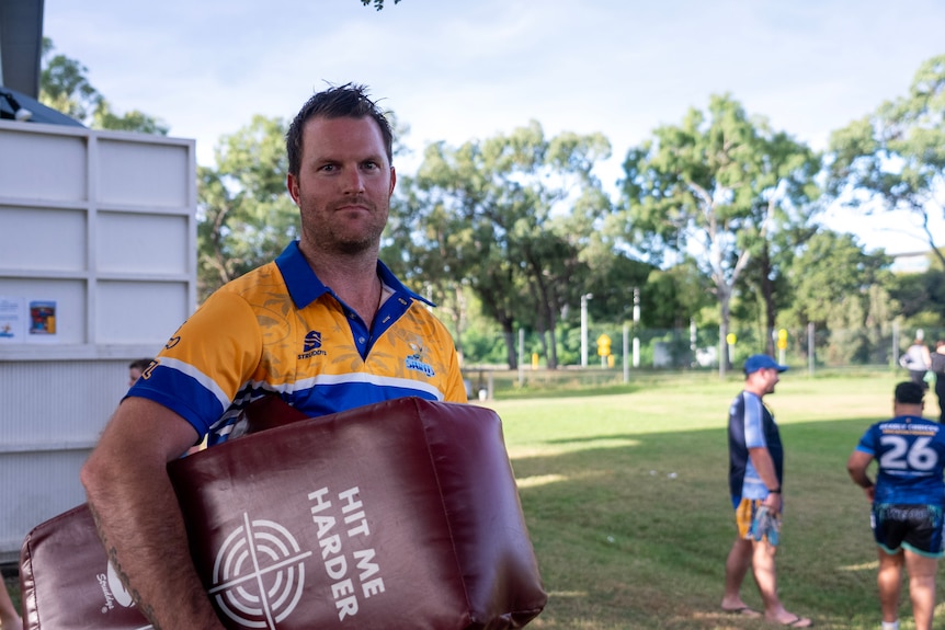 A man in rugby jersey holding a tackle pad on oval and looking to right of frame.