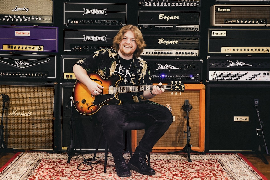 A man sitting in front of a set of speakers playing a guitar