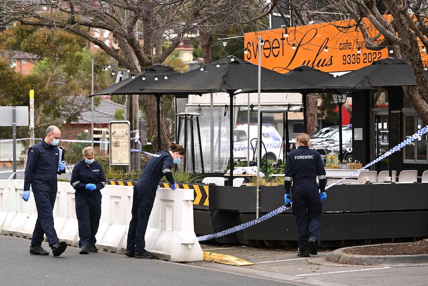 Police officers walk around outside a cafe called "Sweet Lulus" as they investigate a shooting