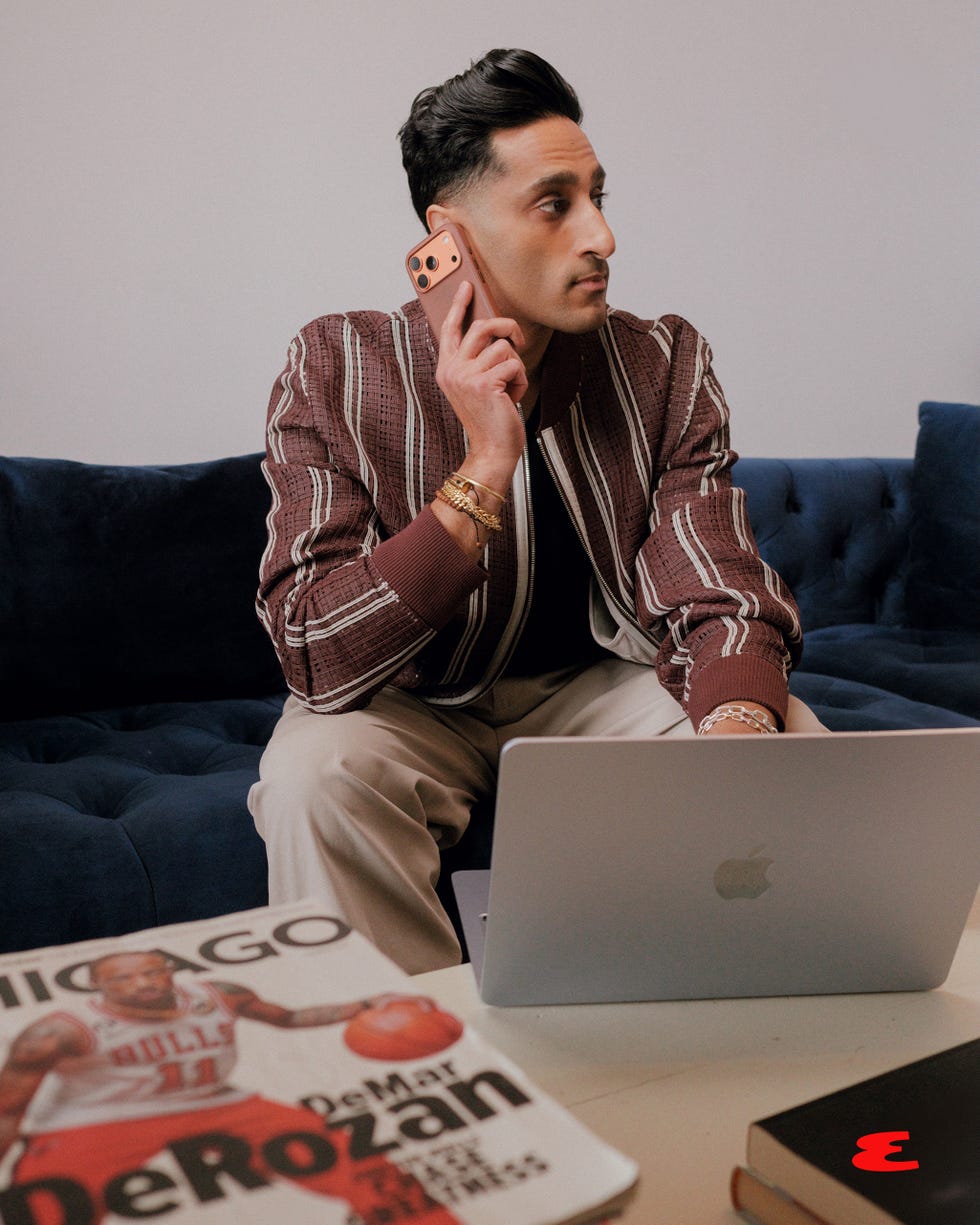 person using a smartphone while seated near a laptop and magazines