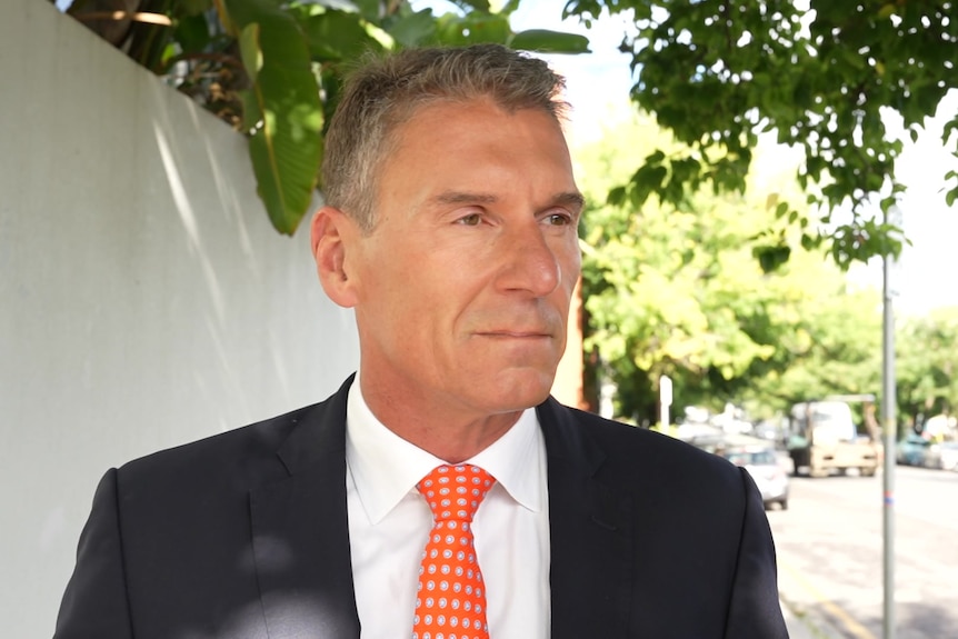 Cory Bernardi on a footpath next to a wall with plant overhanging