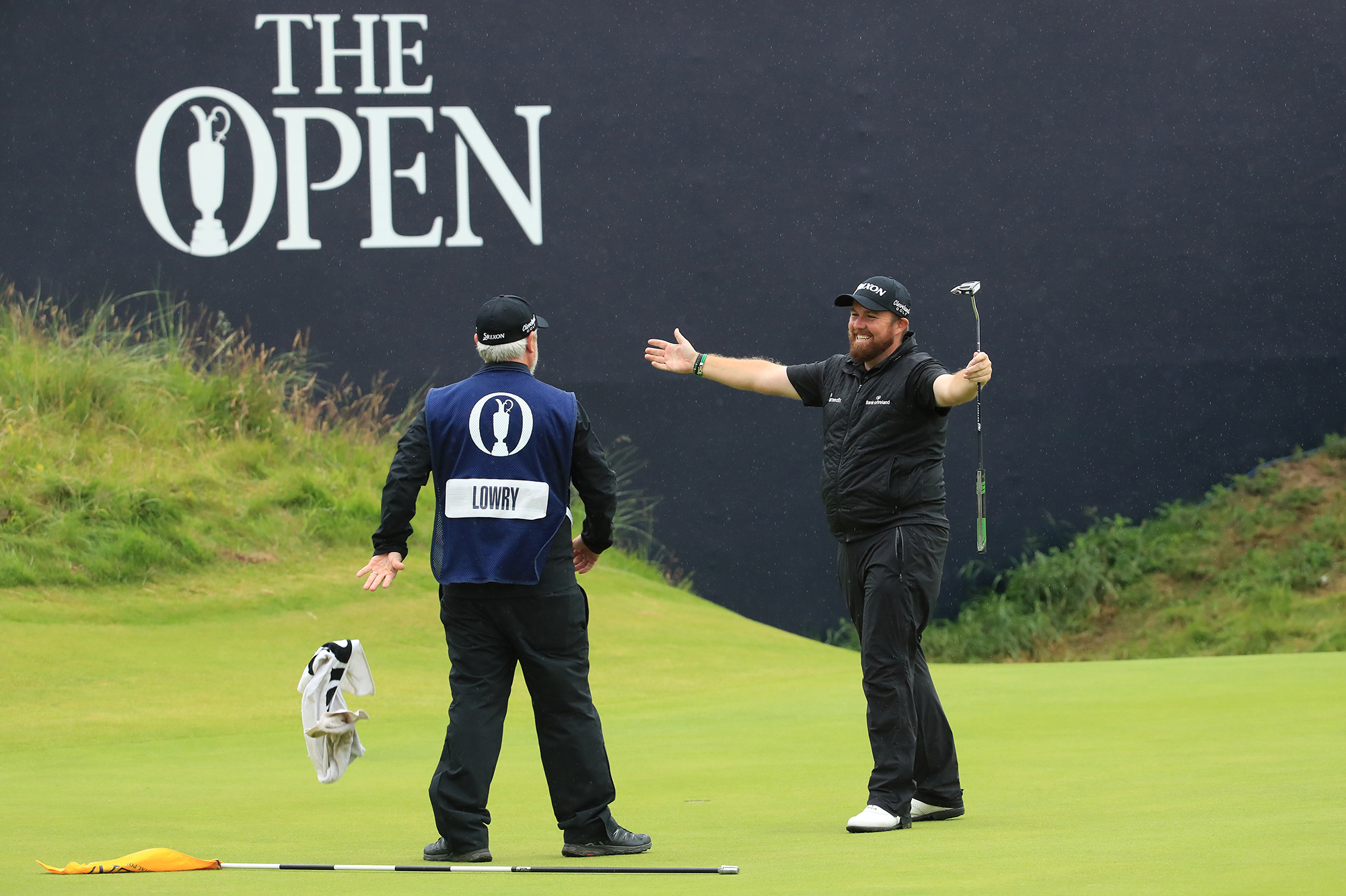 Shane Lowry celebrating with his caddie, with his arms raised in the air jubilantly, after successfully winning the 2019 Open Championship at Royal Portrush