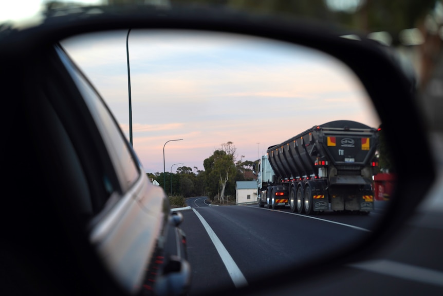 an image of a car's driver side mirror with a truck reflected, driving through a town