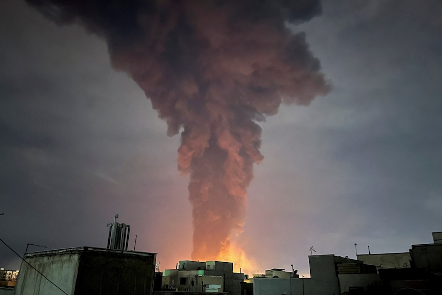 A huge plume  of smoke rises over a city at night.