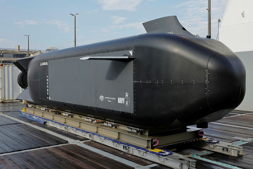 A large black submarine looking vessel on a small platform outside in a dock area. 