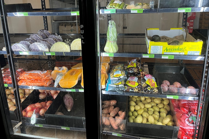 A photo shows fresh produce, including potatoes and pumpkins, behind a glass fridge door in a small supermarket.