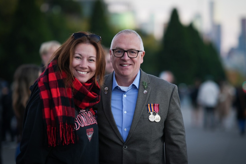Veteran with military medals on suit stands next to wife smiling 
