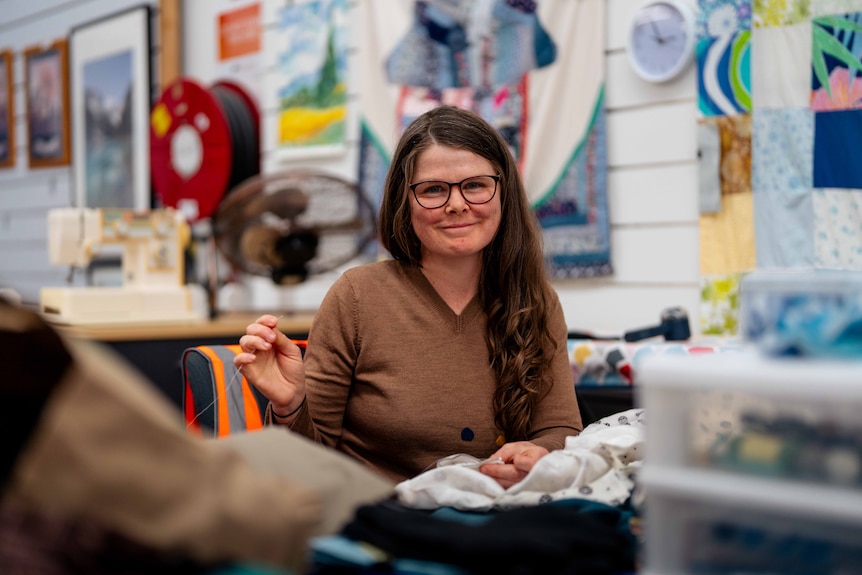 Woman smiles for photo whilst hand sewing