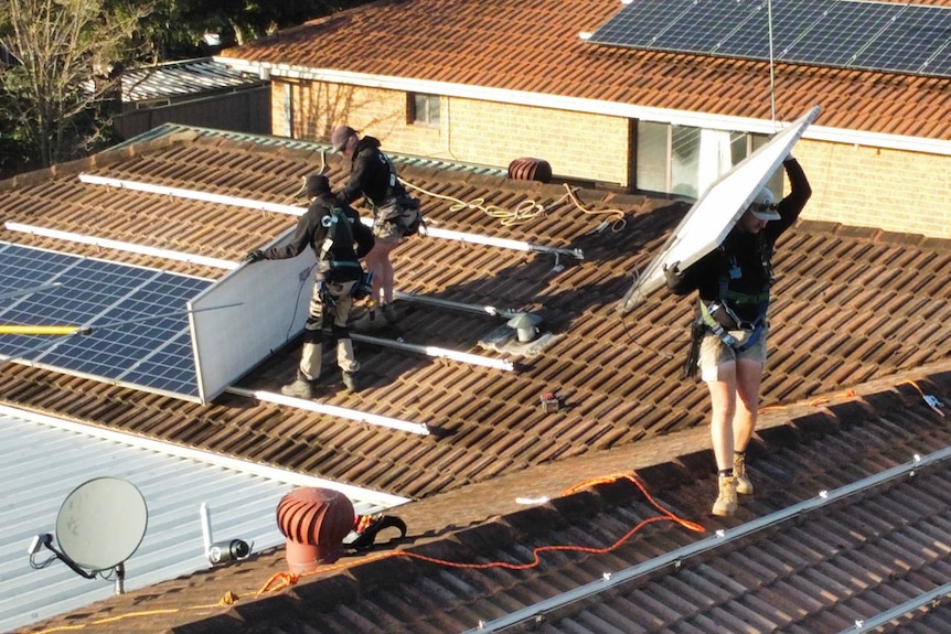 Men in dark clothing standing on a terracotta tiled roof removing solar panels.