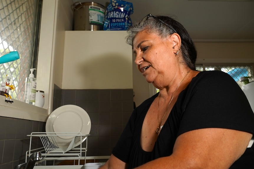 Low angle shot of a woman with tan skin washing dishes at a kitchen sink.