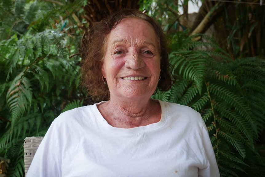 A cropped pic of a lady in a while tshirt with garden greenery in the background.