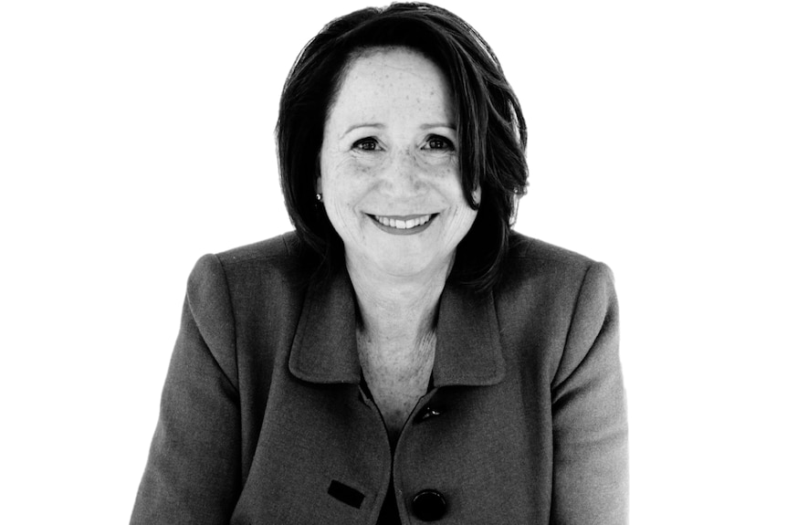 A black and white photo of an older woman with a dark bob smiling. She is wearing a professional collared jacket.