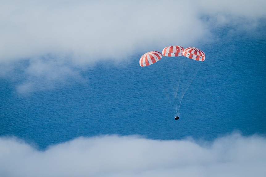 The Orion space capsule floats over the ocean, slowed down by balloons.