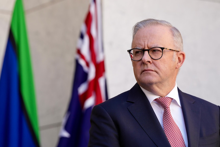 A man in a suit looks across the camera with an australian flag in the background.