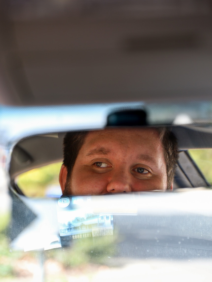 Car rearvision mirror shows man's eyes staring out toward street.