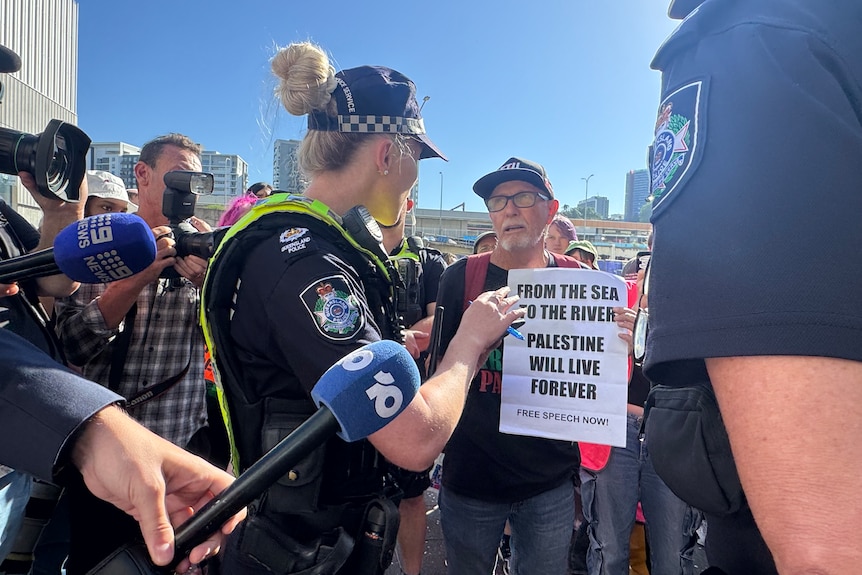 A man holds a sign that reads "from the sea to the river palestine will live forever" while talking to a police officer