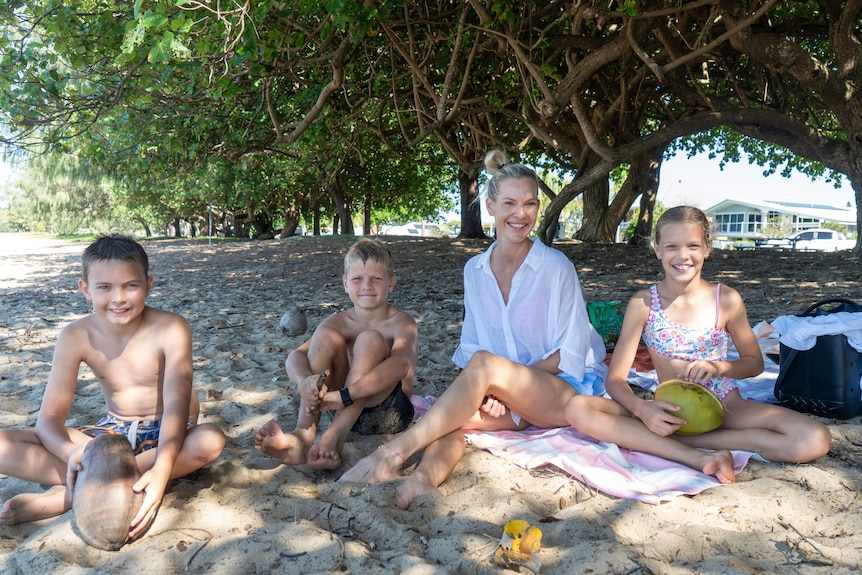 A smiling woman, two boys and a young girl sit on a beach.