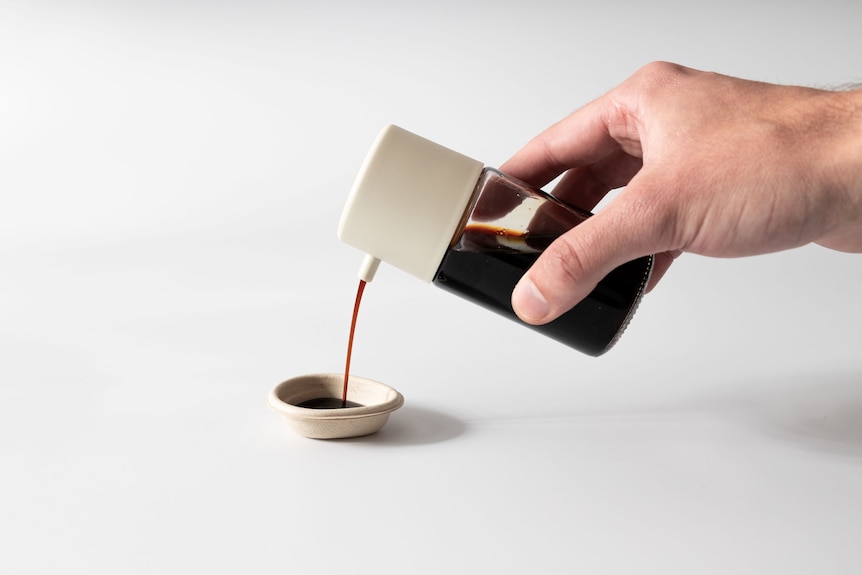 A hand pouring soy sauce from a bottle into a small dish.