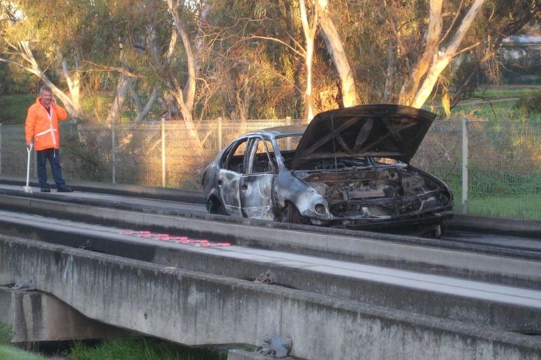 A burnt-out car on a concrete bus track