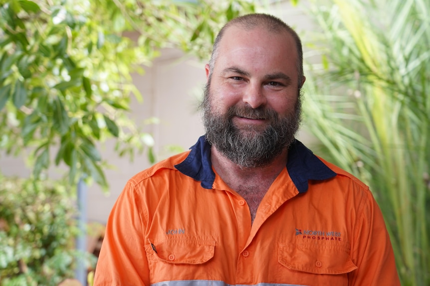A man with a beard smiles, in orange hi vis work shirt