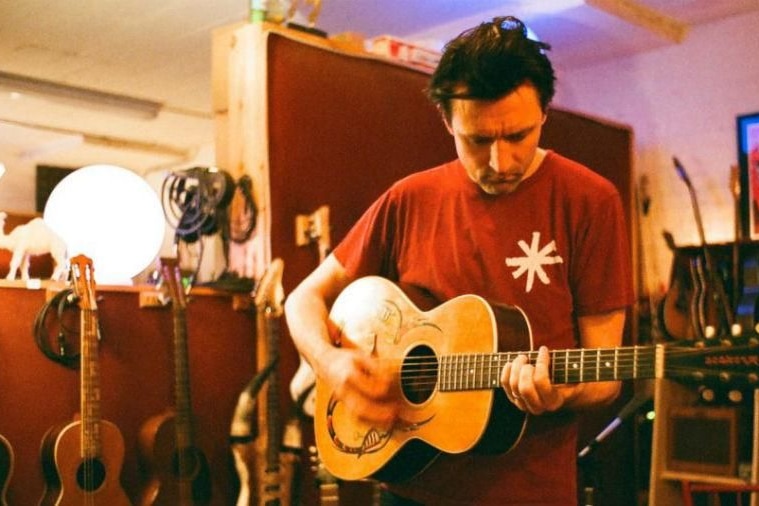 A dark-haired man plays an acoustic guitar in a recording studio.