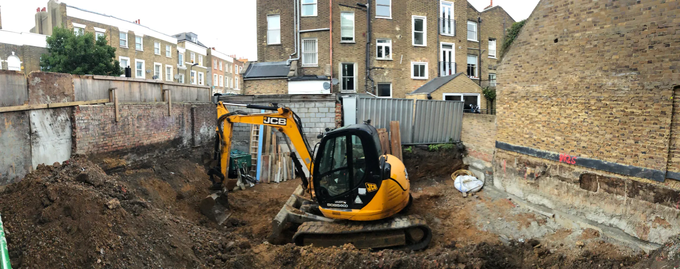 A yellow excavator digging a foundation pit for a new building.