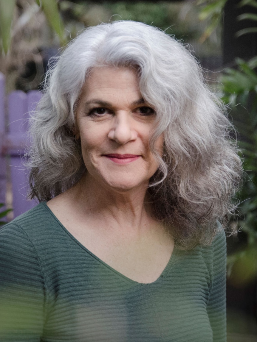 A woman with long wavy grey hair, wearing a green top, looking at the camera.