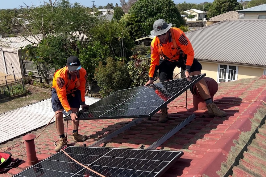Two men install a solar panel on a rooftop.