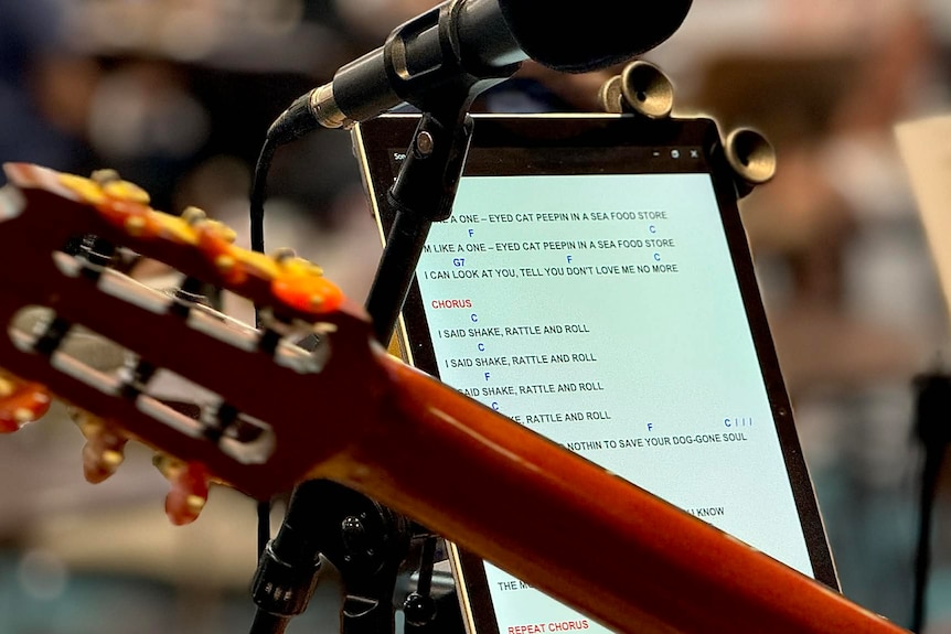 A close-up of a ukulele and and ipad with words and chords on the screen.