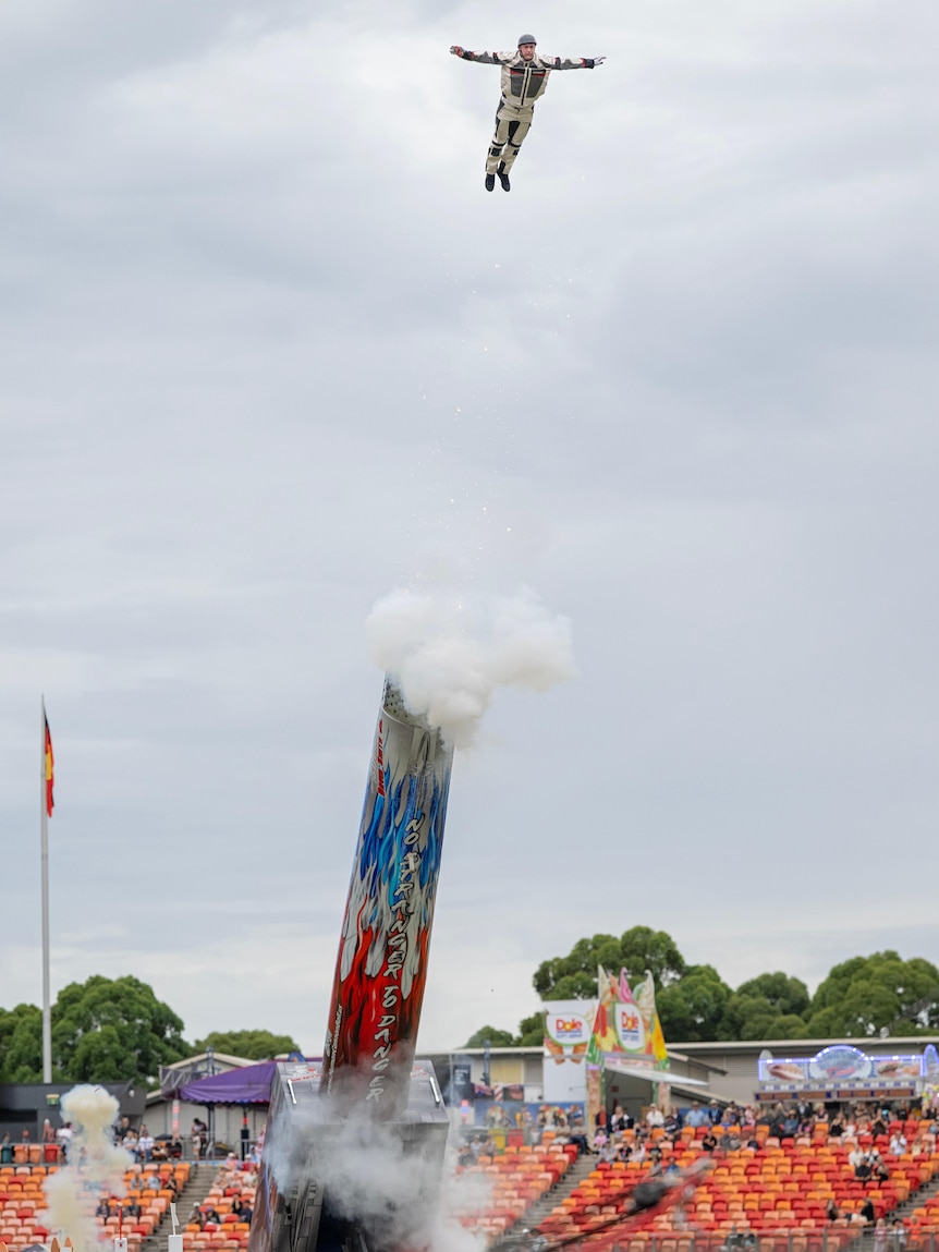A man flies with his arms spread out above a large smoking cannon.