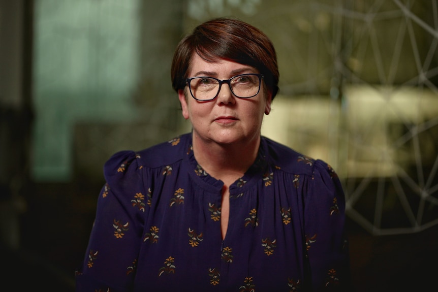 a woman with short hair and black glasses looking seriousy into the camera