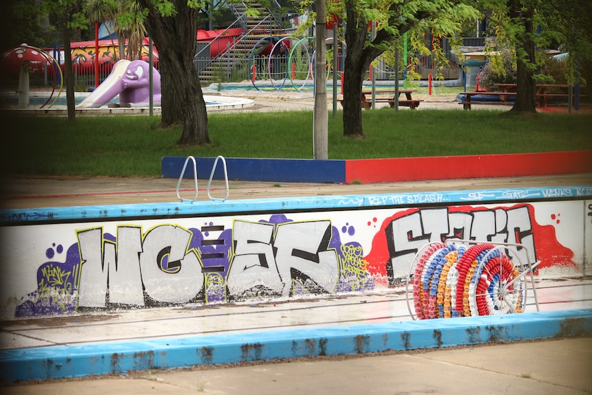 Graffiti sprayed on the wall of an emptied swimming pool at a waterpark in a state of significant disrepair.