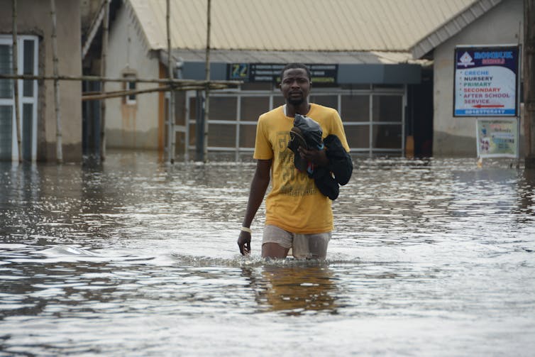 man in yellow shirt walks through flooded street