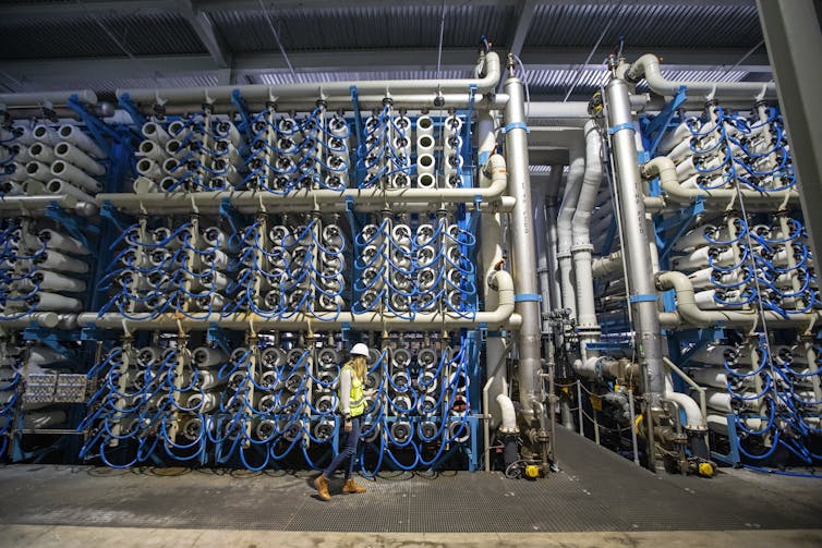 A woman in a hardhat walks past stacks of tubes for making saltwater drinkable.