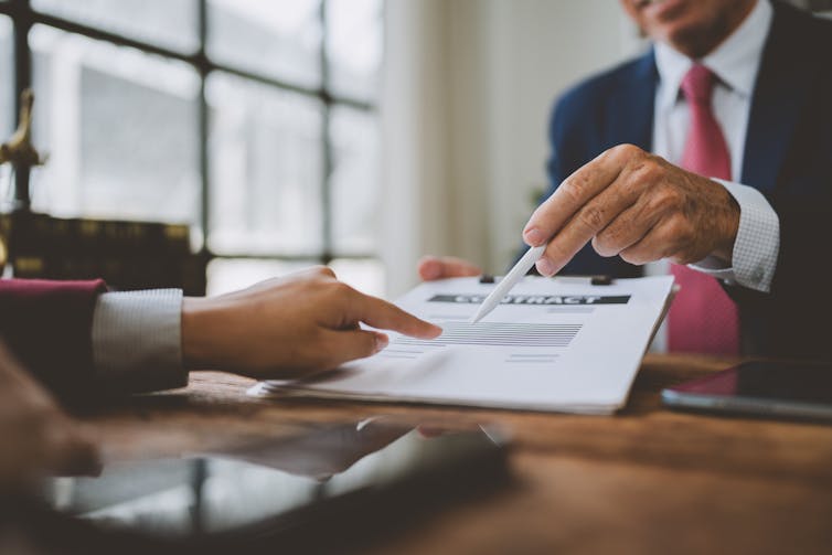 someone pointing to a  section of a contract while another person offers them a pen.