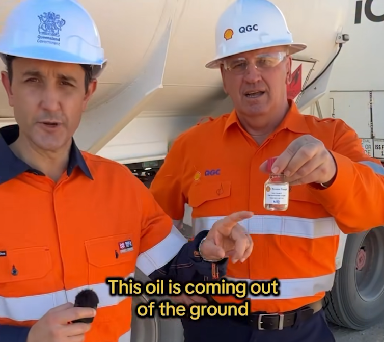 two men in high vis vests holding a sample of oil next to an oil tanker.