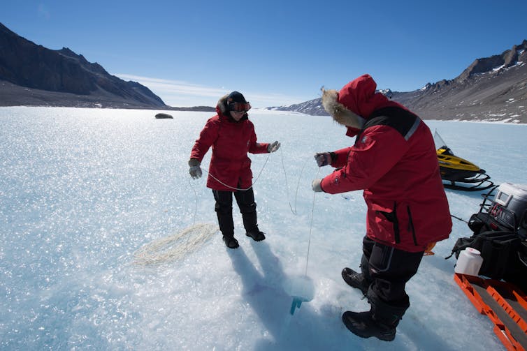Two people in red snow coats on a frozen lake with deep blue sky in the background.