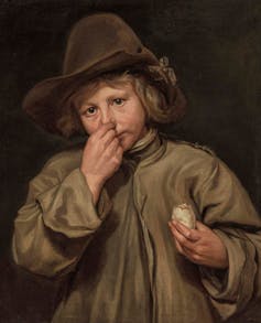A boy holding a rotten egg and his nose.